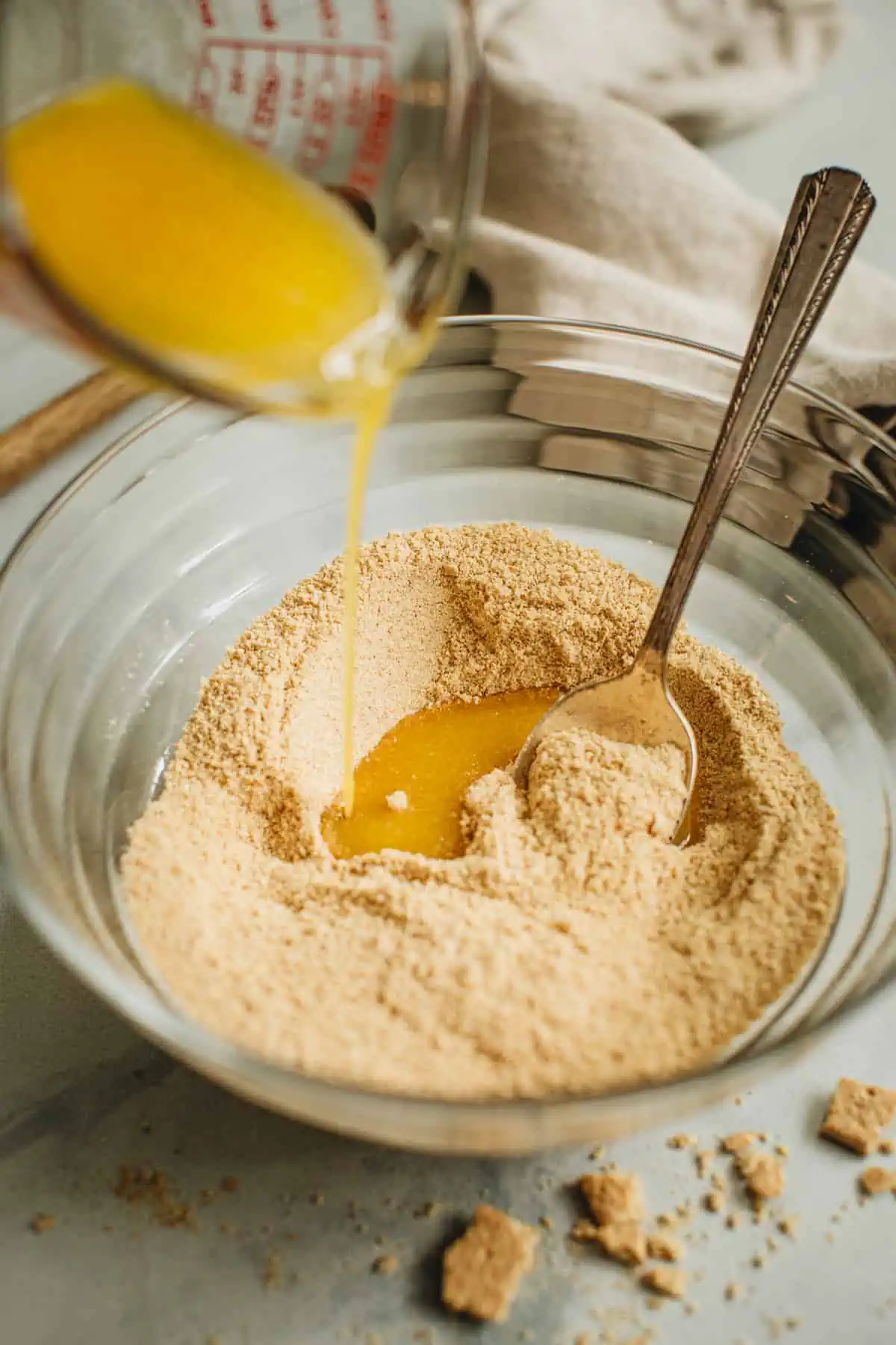 Pouring butter into the crumb mixture to make Graham Cracker Crumb Crust.