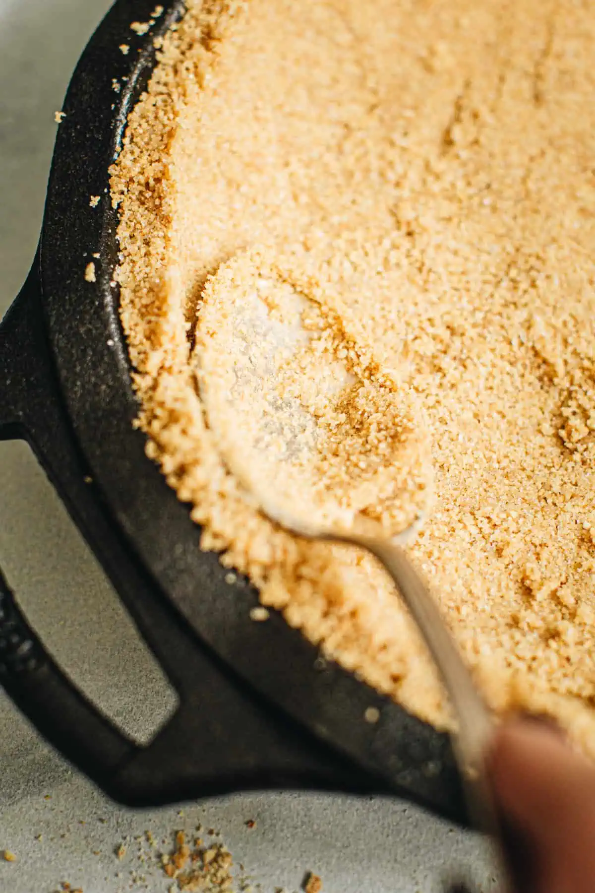 Spoon pressing into the crumbs to form the graham cracker crumb crust.