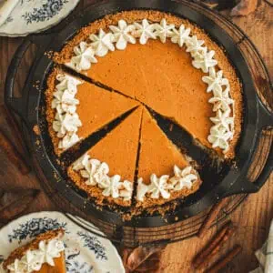 Sliced sweet potato pie in graham cracker crust with whipped cream on top.