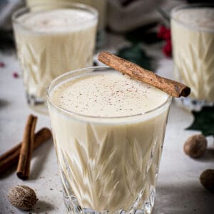 Homemade eggnog topped with freshly grated nutmeg in a glass with a cinnamon stick on top.