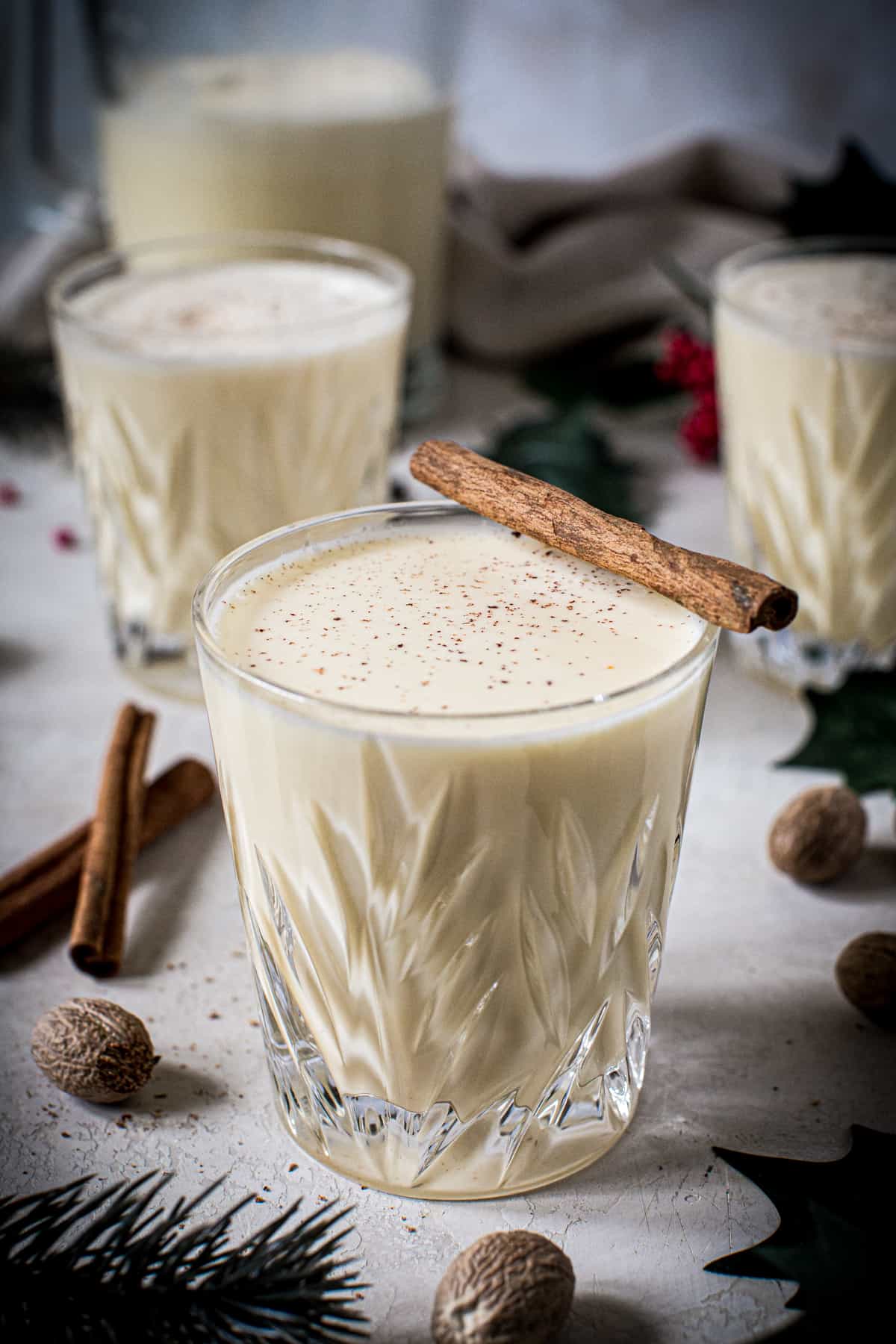 Homemade eggnog in a glass topped with a cinnamon stick and freshly grated nutmeg.