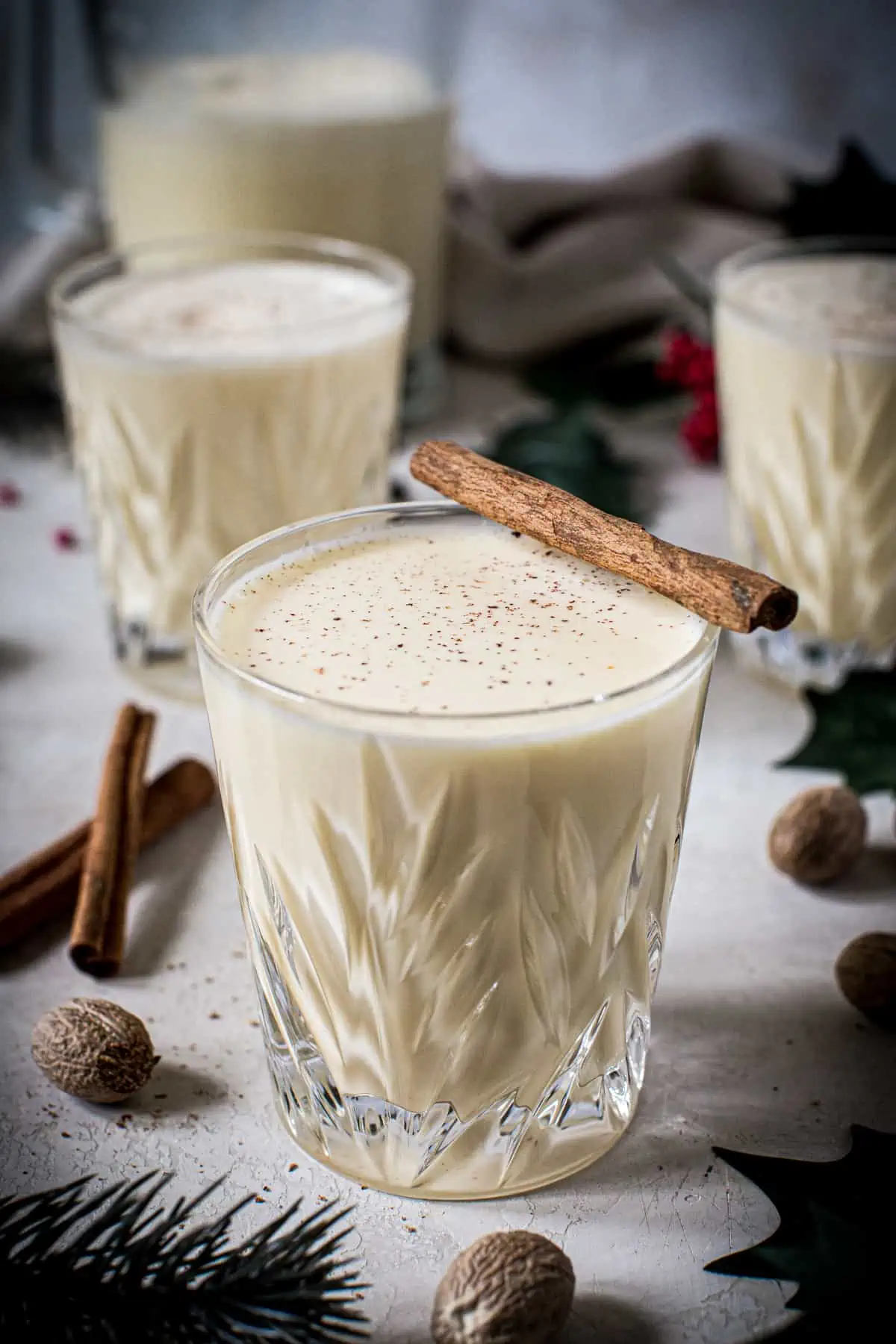 Homemade eggnog topped with freshly grated nutmeg in a glass with a cinnamon stick on top.