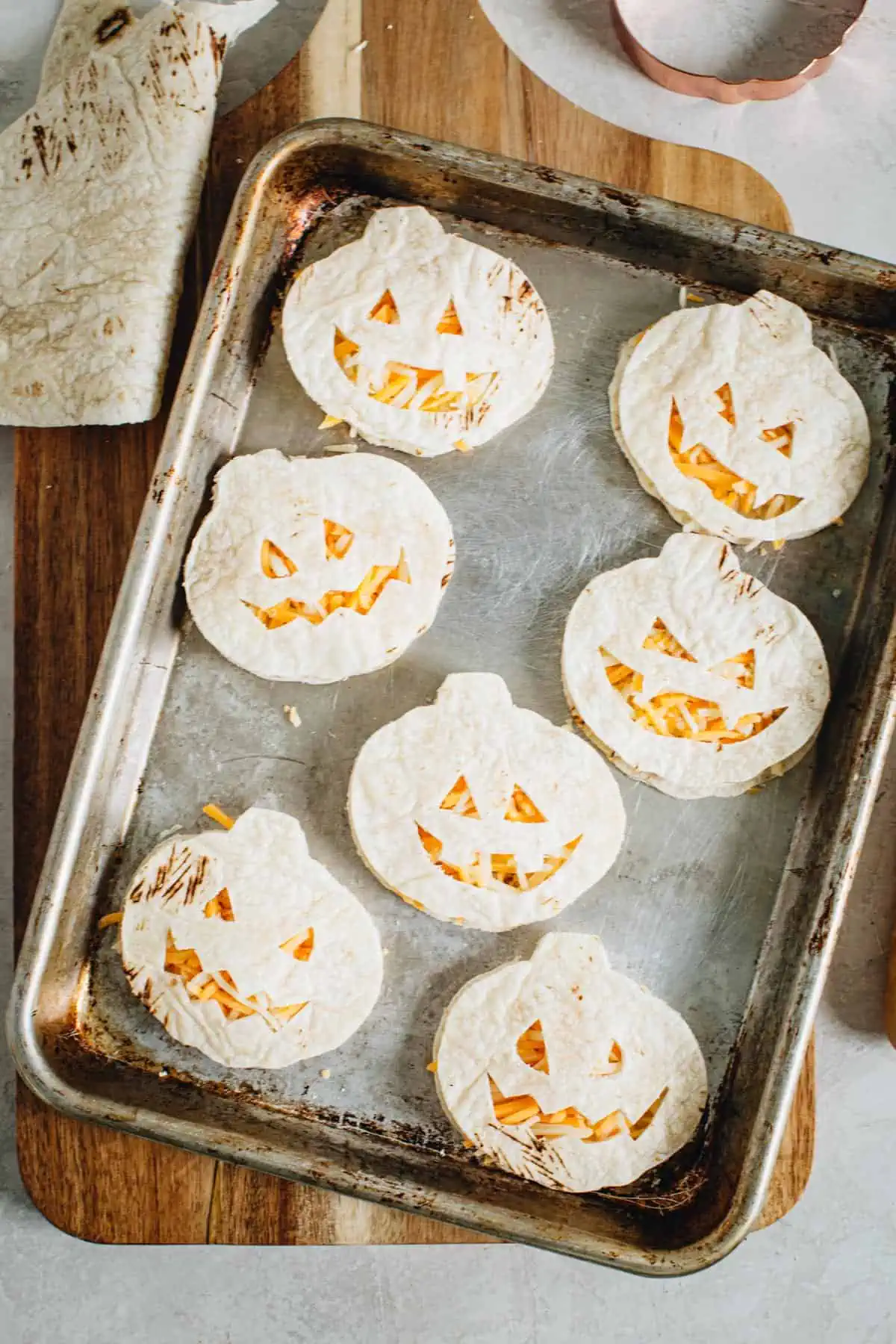 Unbaked jack-o-lantern quesadillas on a rimmed baking sheet.