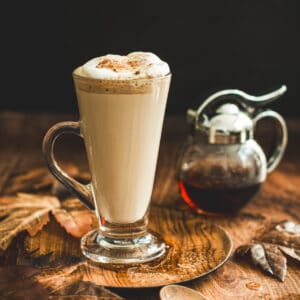 Maple latte in a tall glass mug with foam on top.