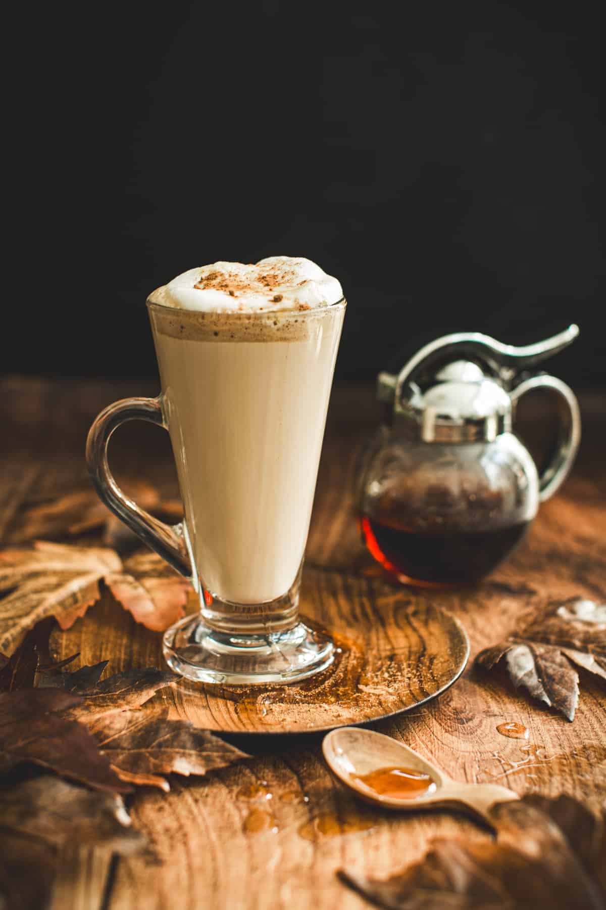 Maple latte in a tall slim glass mug with a dusting of cinnamon on top of the foam.