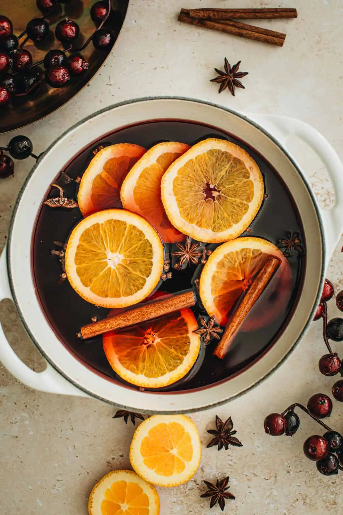 Wine, brandy, orange slices, and whole spices in a pot for making traditional mulled wine.