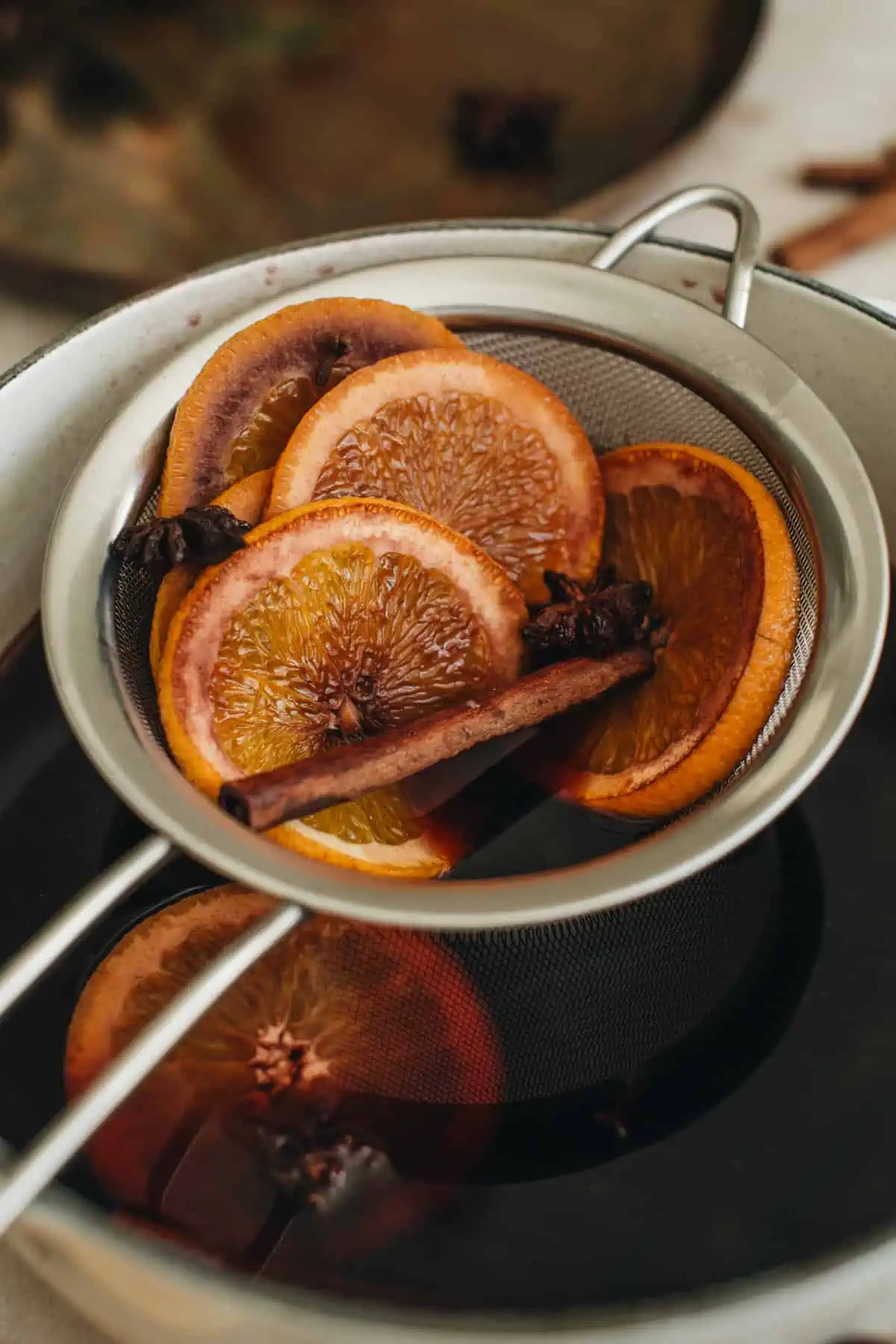 Strained orange slices and whole spices sitting over the pot of mulled wine.