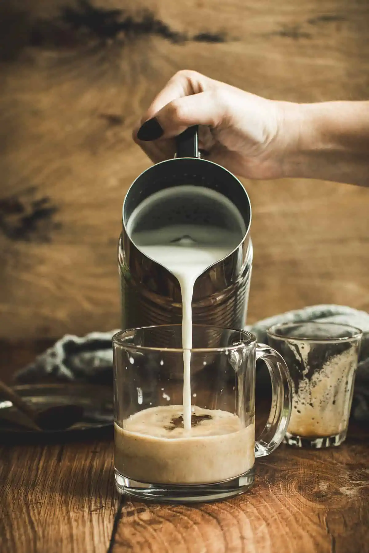 Pouring steamed milk over pistachio latte ingredients in a coffee mug.