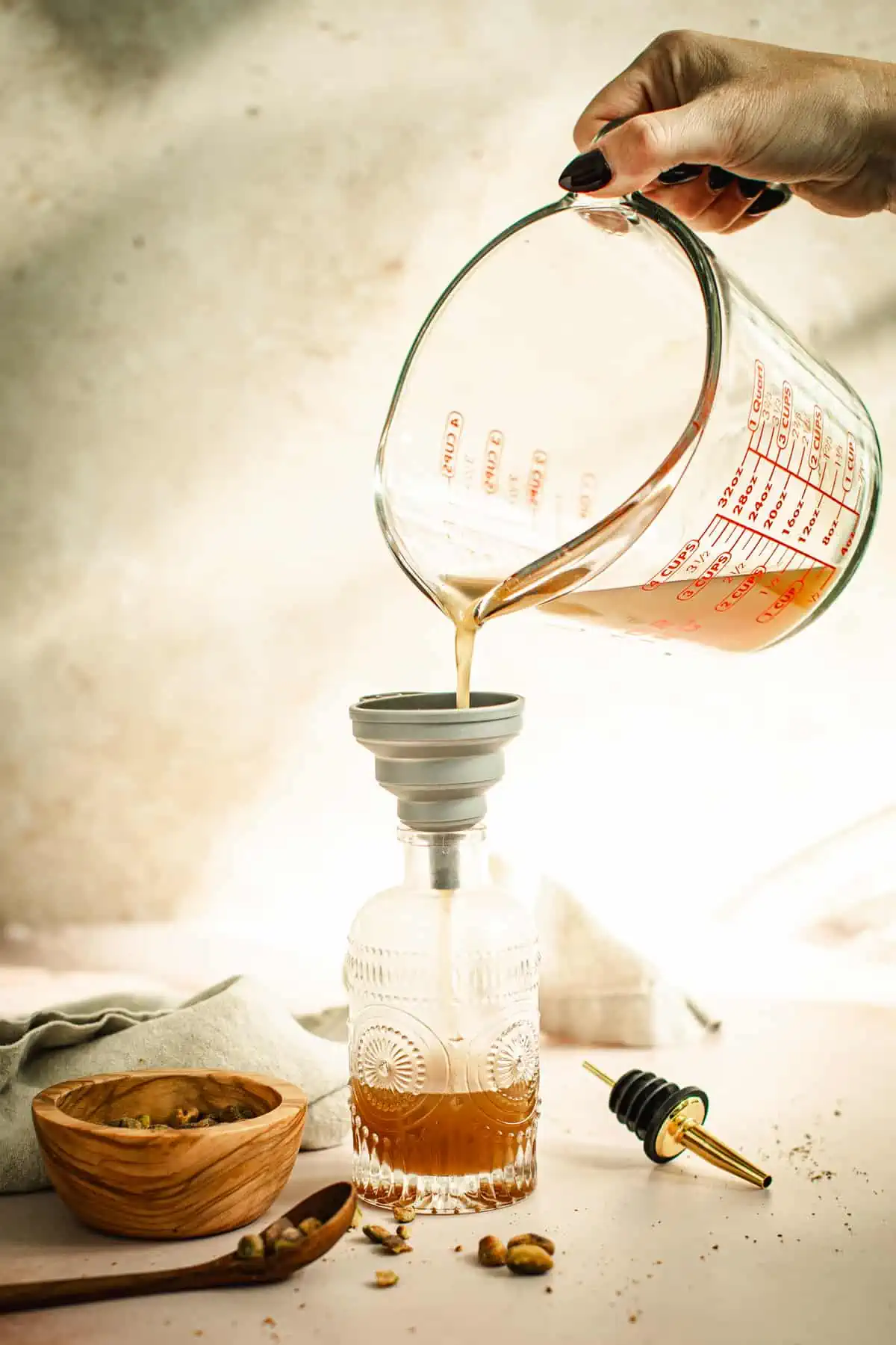 Pouring pistachio syrup from a measuring cup into a decorated glass bottle.