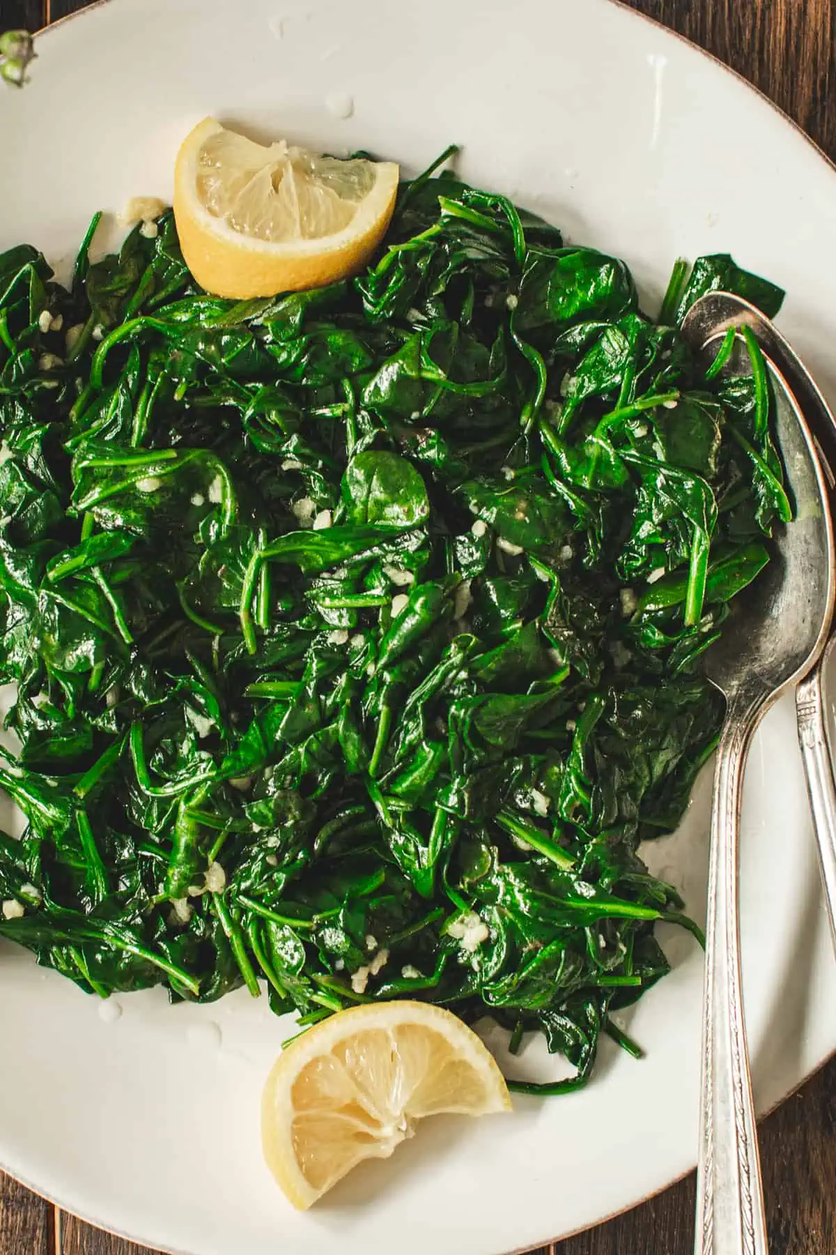 Sautéed spinach with lemon and two serving spoons on a white plate.