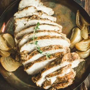 Sliced slow cooker turkey breast on a platter with roasted onions around it.