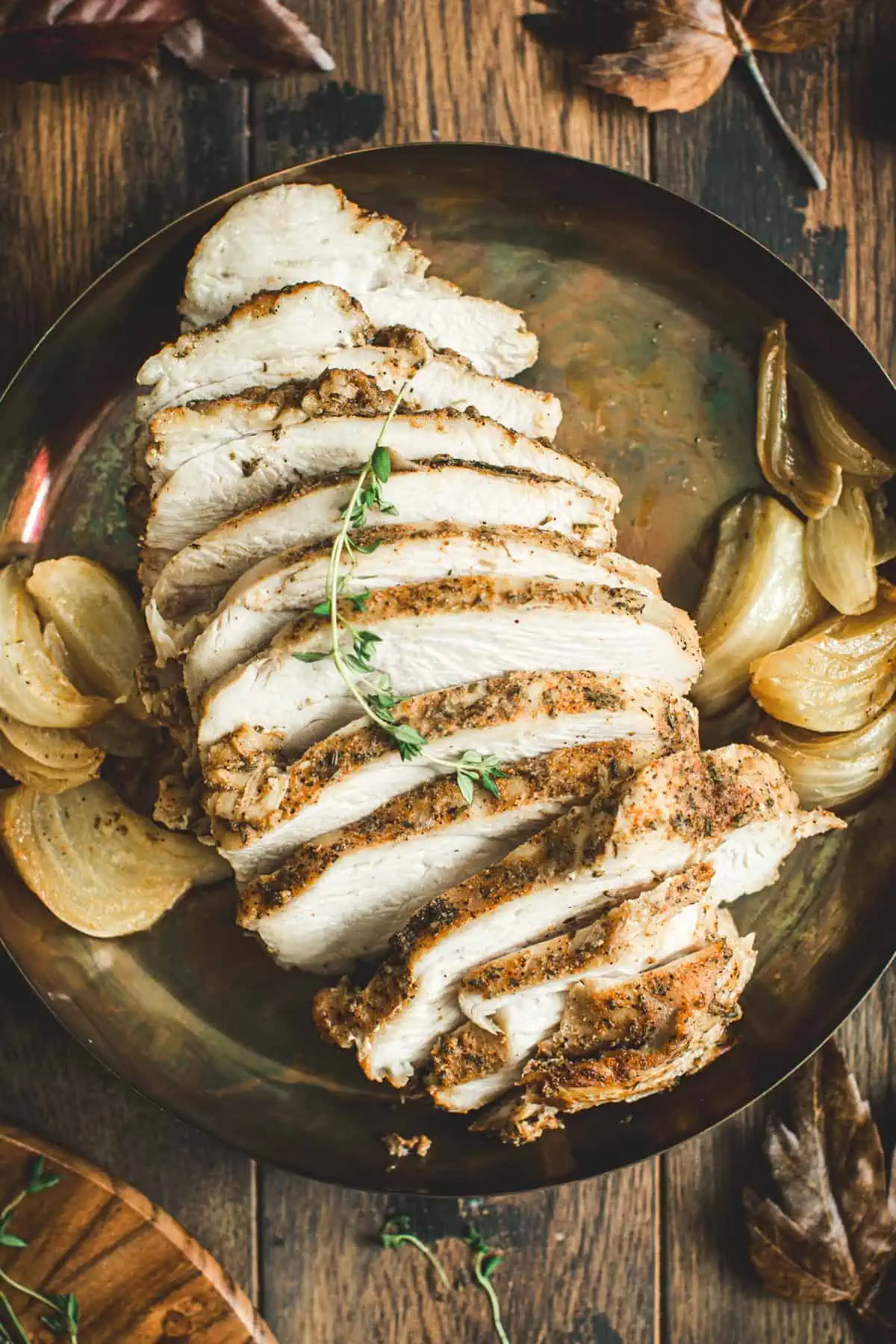 Sliced Slow Cooker turkey breast on a round serving tray with roasted onions around it.