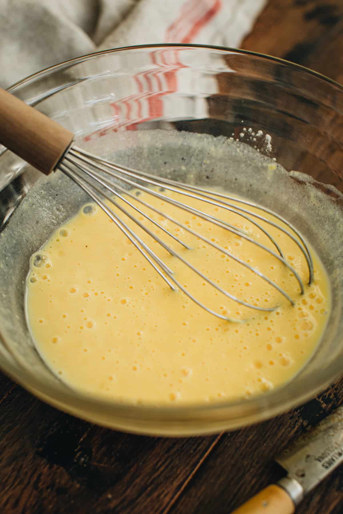 Vanilla pudding mixed with milk in a mixing bowl with a wire whisk inside.