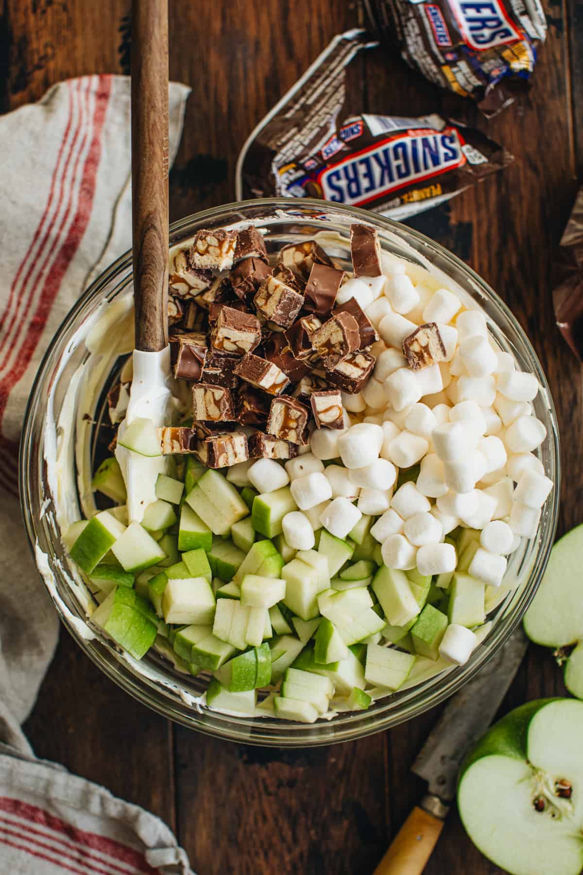 Chopped apples, Snickers, and mini marshmallows on top of the pudding mixture for Snickers Salad in a mixing bowl.