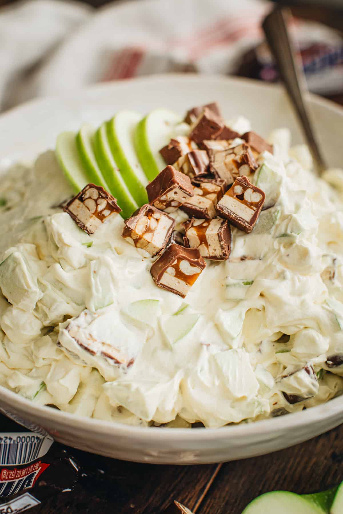 Snickers salad in a white bowl topped with apple slices and chopped snickers bars.