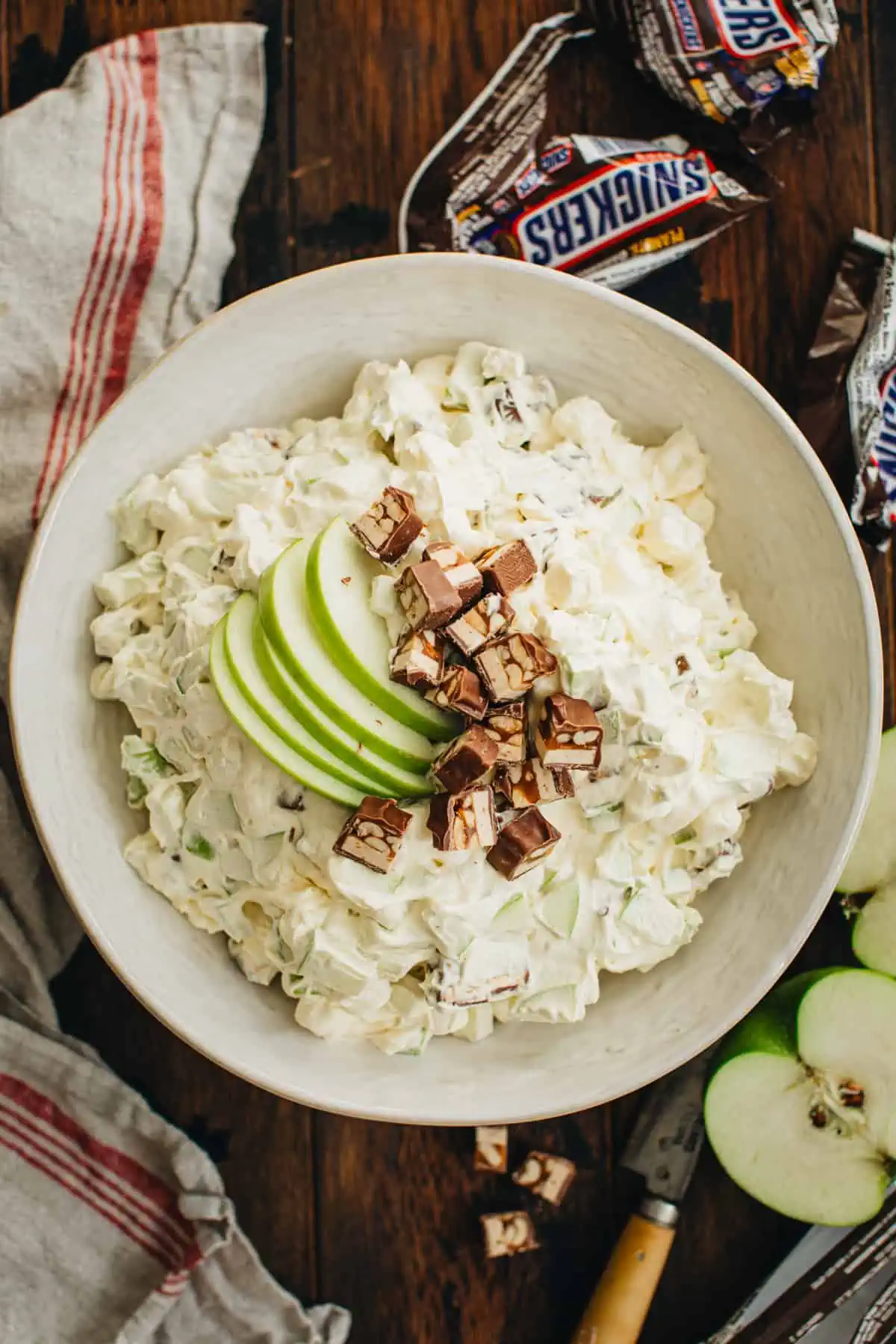 Snickers Salad in a white bowl topped with sliced apples and chopped Snickers.