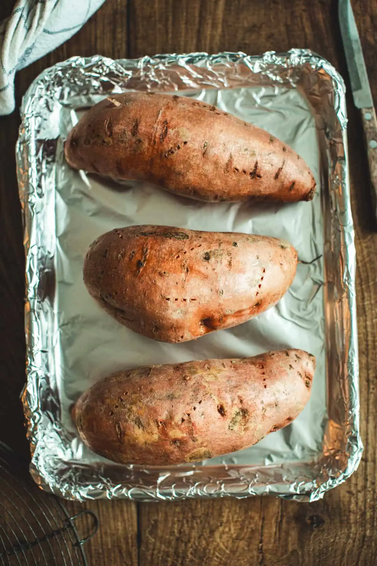 Pierced sweet potatoes on a foil-lined baking sheet for making graham cracker crust sweet potato pie.