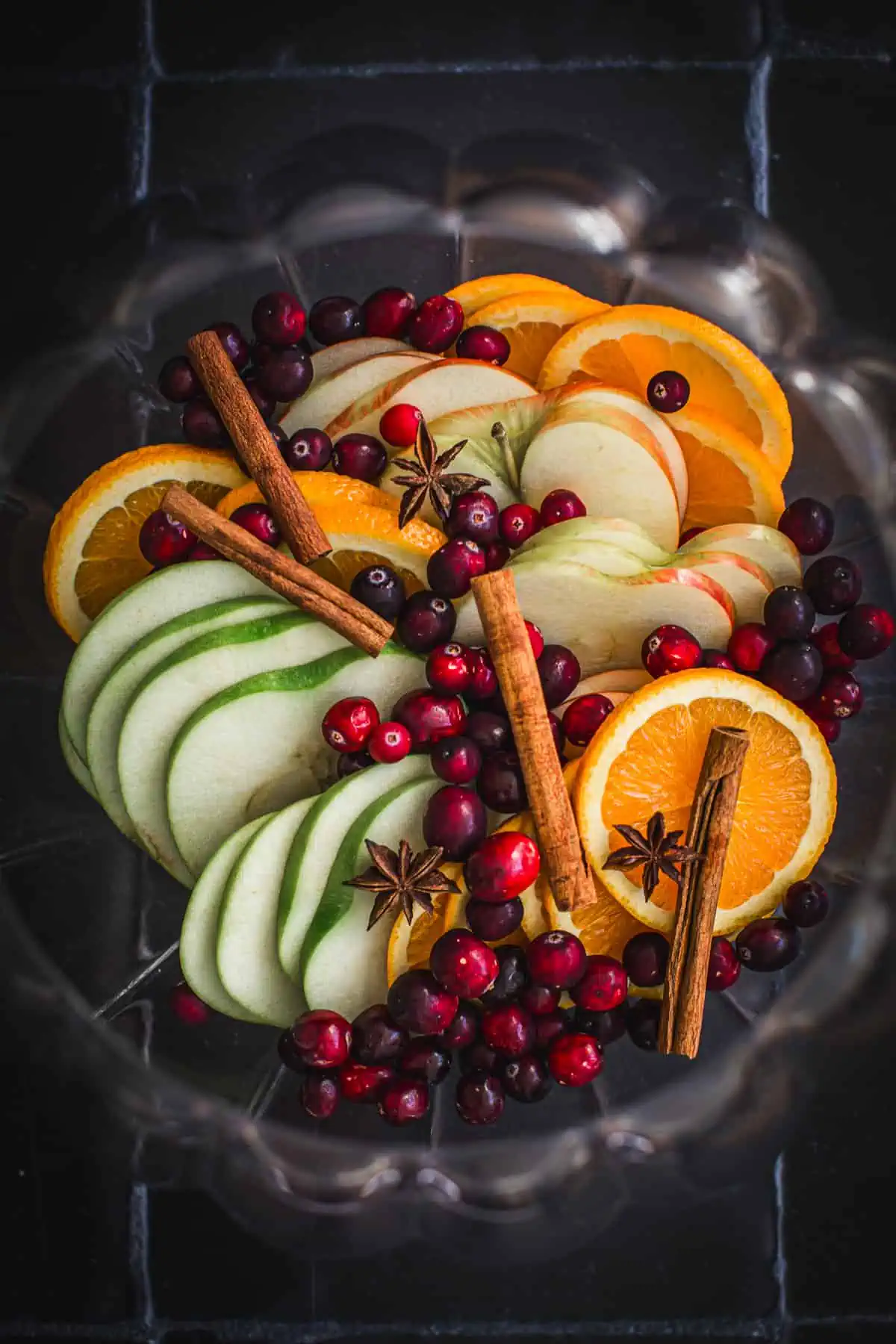 Fresh fruit slices, cranberries, cinnamon sticks, and star anise in a punch bowl for making Thanksgiving sangria.