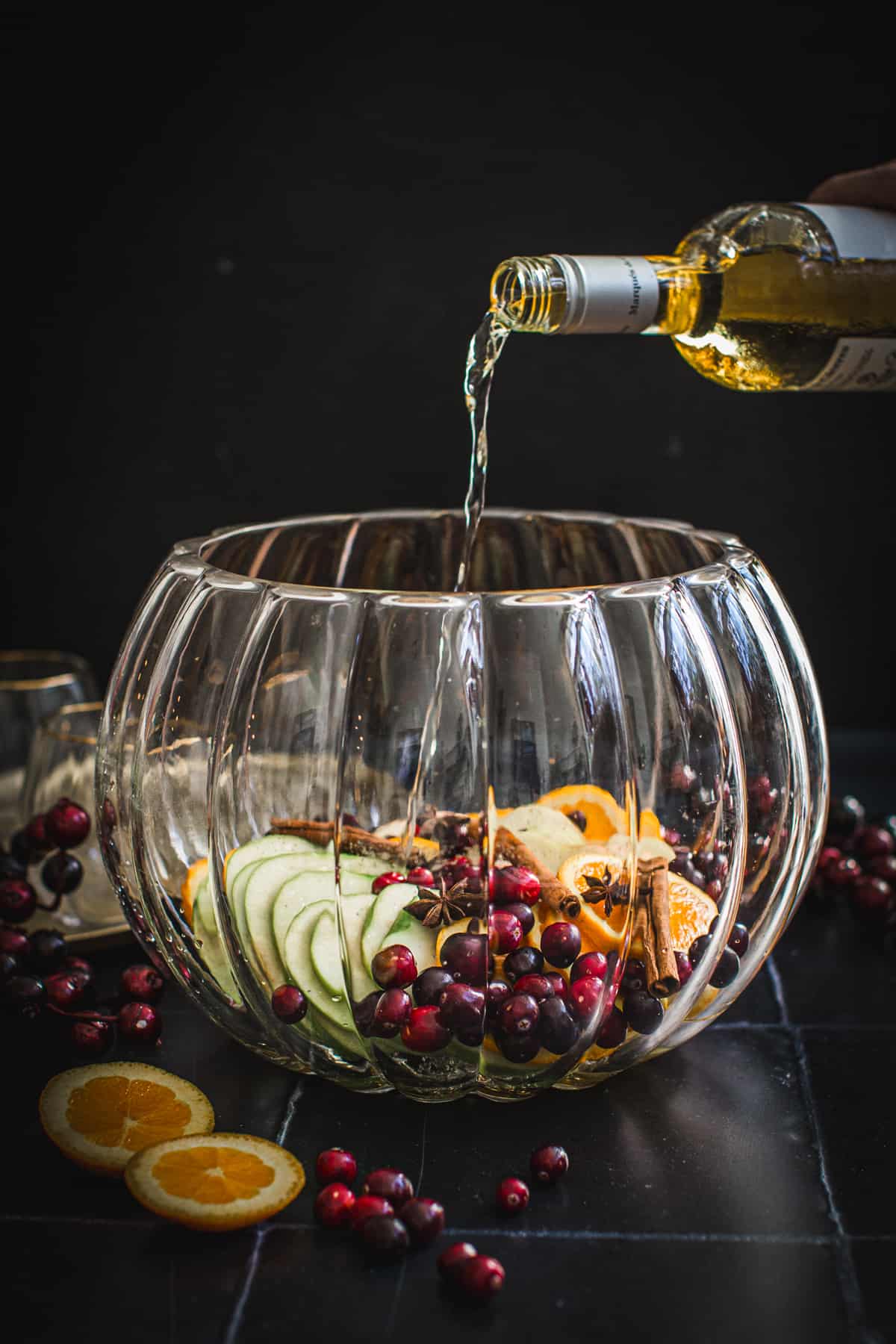 Pouring wine into a punch bowl over the fresh fruit and spices for Thanksgiving sangrial
