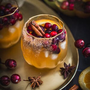 Thanksgiving sangria in a pumpkin-shaped glass with fresh cranberries, and orange slice, and a cinnamon stick.