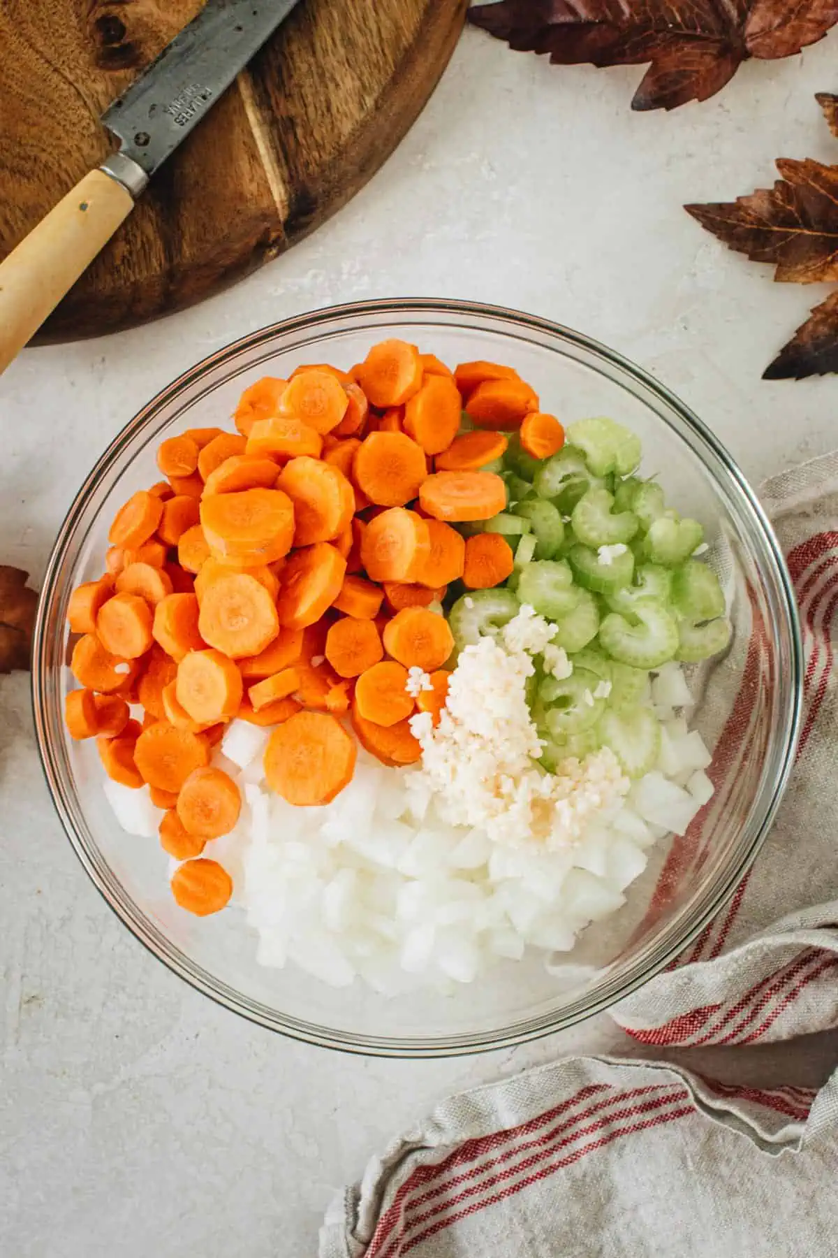 Chopped carrots, celery, onions, and minced garlic in a bowl for making Tuscan white bean soup.