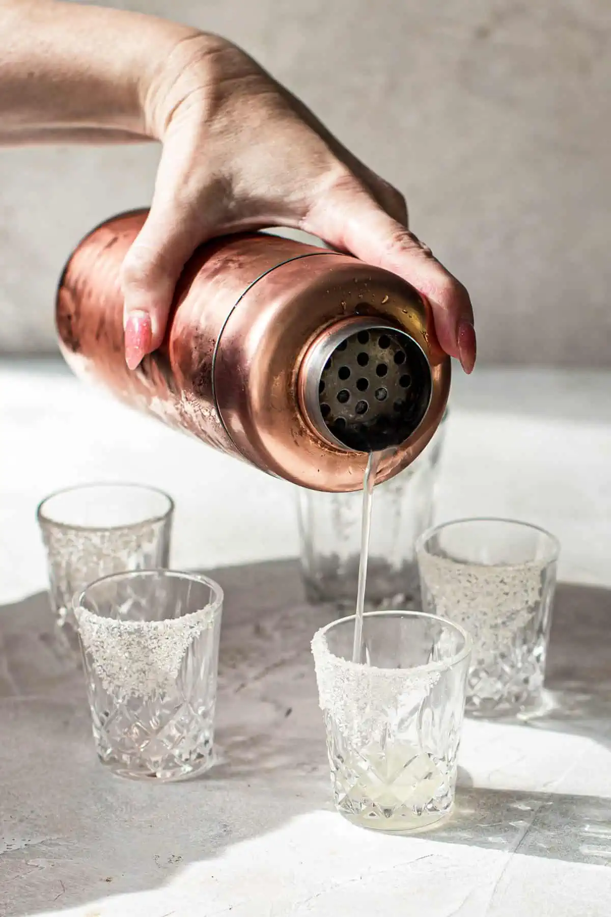 Straining white gummy bear shots into shot glasses.