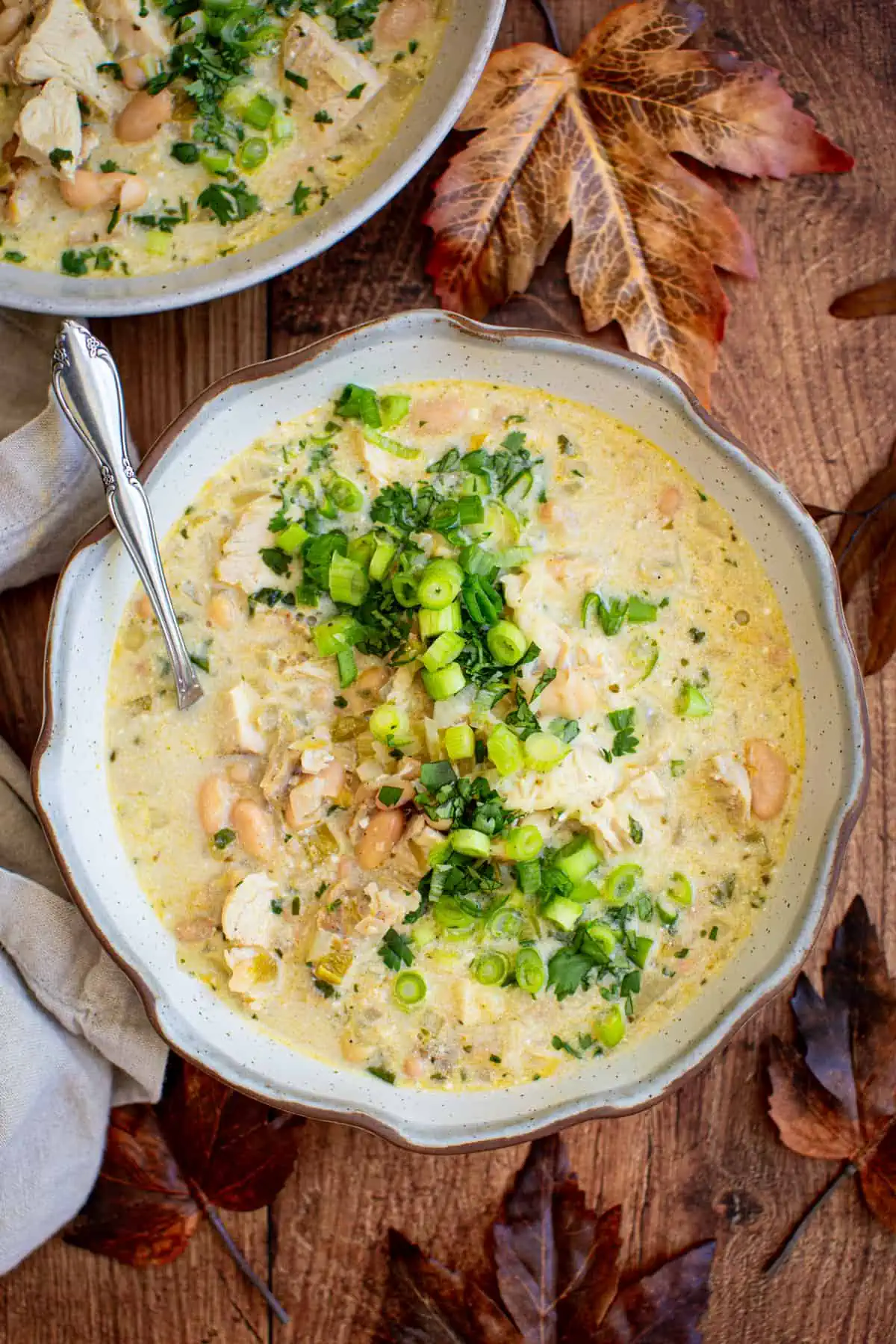 White turkey chili topped with fresh cilantro and green onions in a bowl with a spoon.