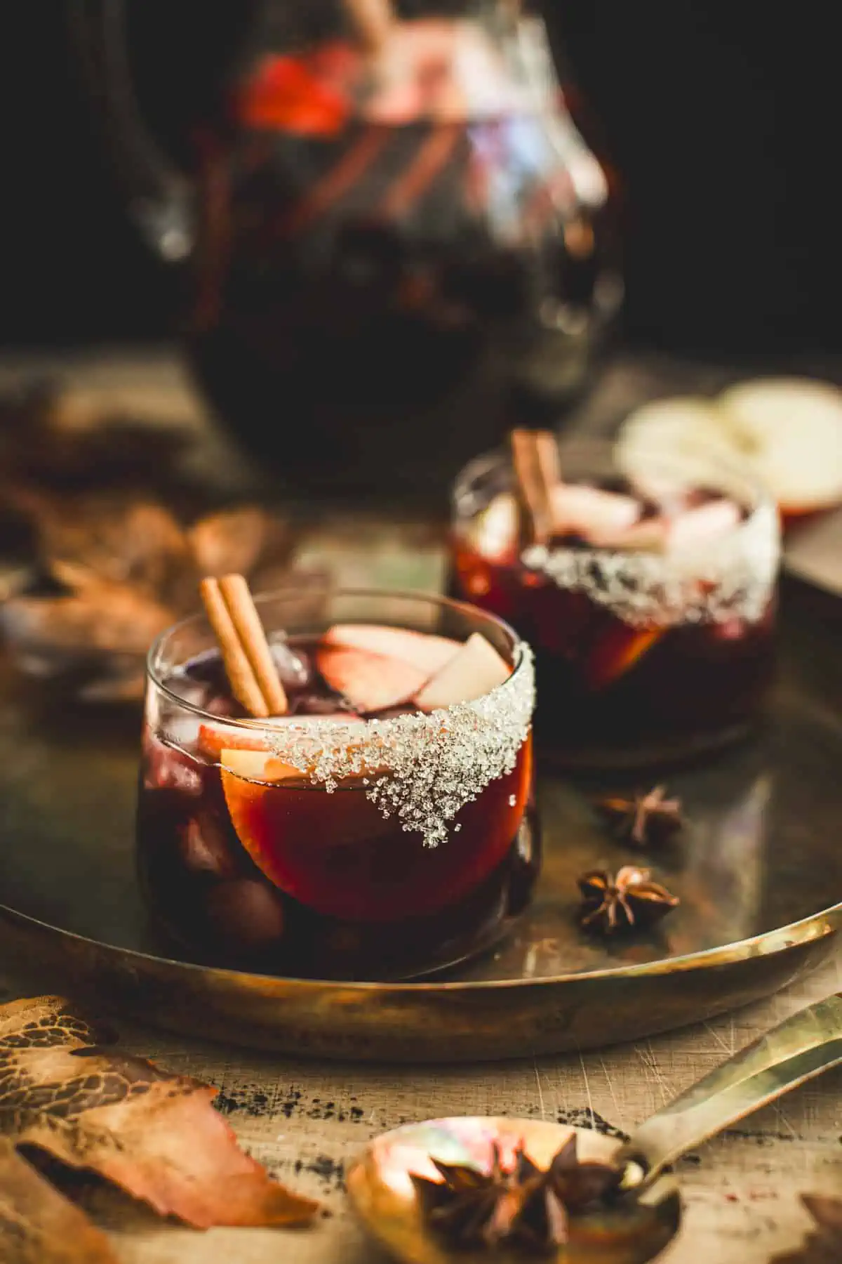 Apple Sangira in a short glass with a sugared rim and fruit with cinnamon sticks for garnish.