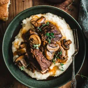 Braised short ribs over mashed potatoes in a green bowl.