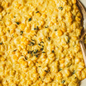 Creamed corn topped with fresh thyme in a white bowl with a silver serving spoon.