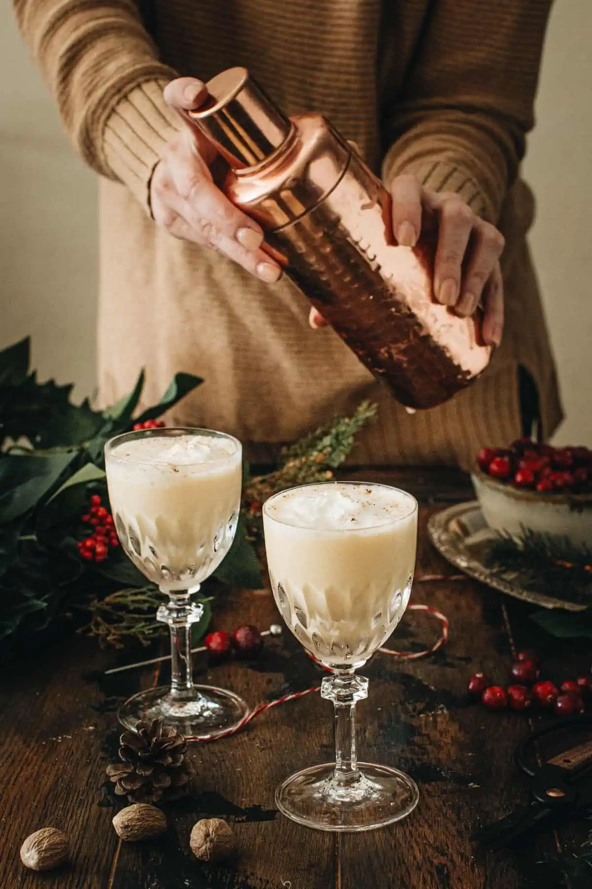 Person holding a copper cocktail shaker over two eggnog martinis.