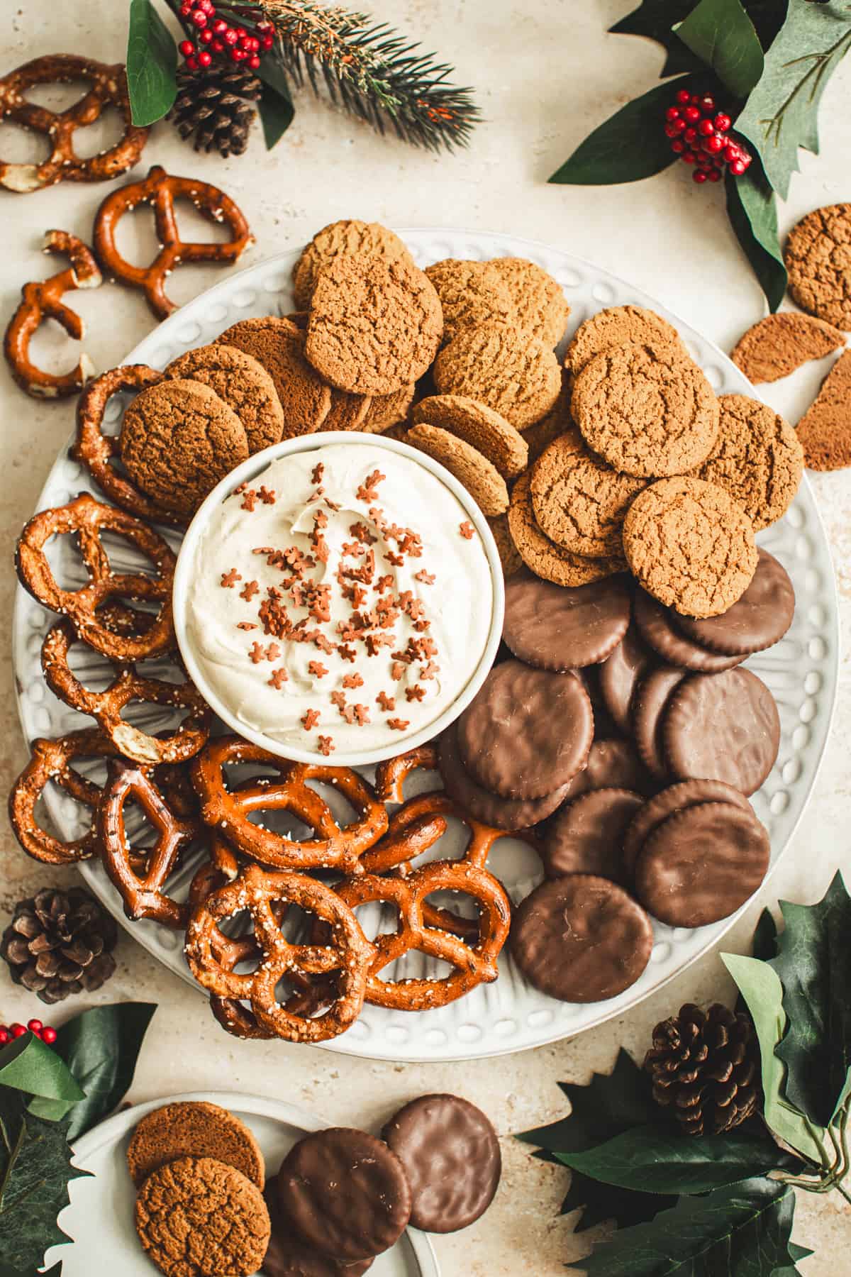 Gingerbread dip topped with candy gingerbread men and on plate with ginger snaps, pretzels, and chocolate crackers.