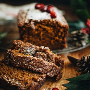 First three slices of gingerbread loaf laying on each other with the gingerbread loaf behind it on a round wire rack.