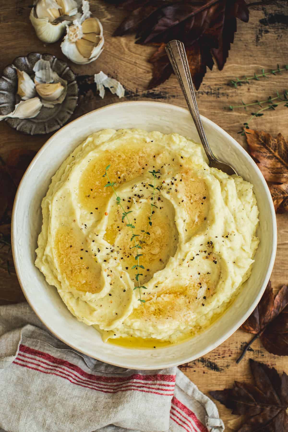 Mashed potatoes with truffle in a white bowl topped with melted butter and fresh thyme with a serving spoon.