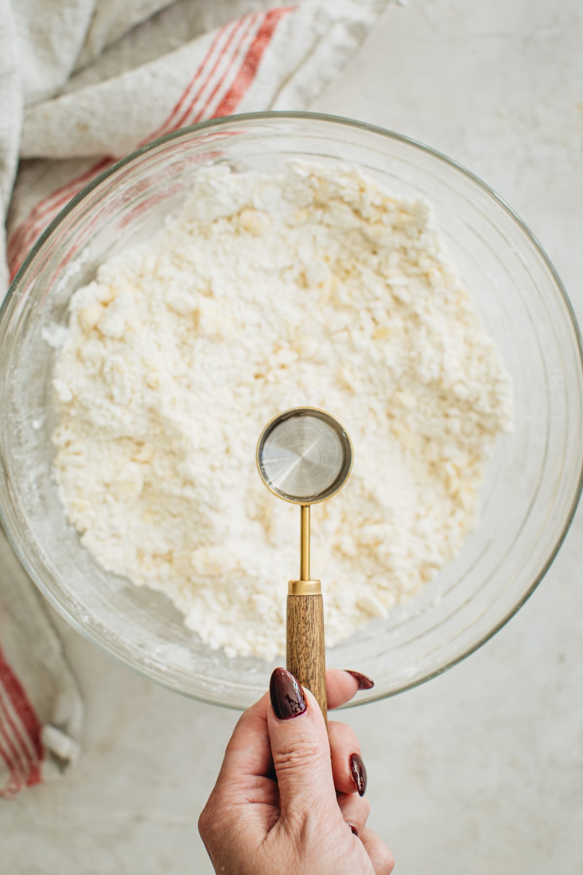 Tablespoon holding water over the pie dough for making a pie crust with shortening.