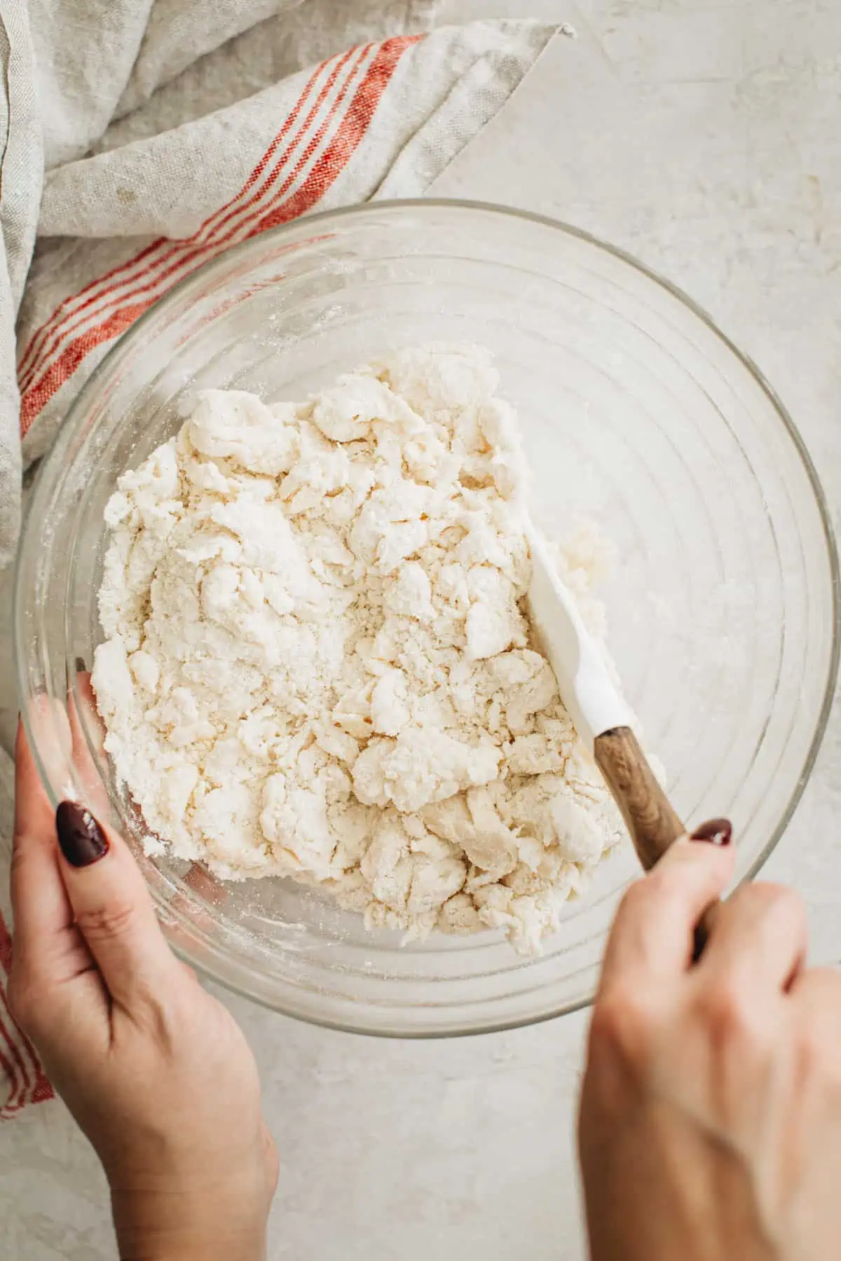 Using a rubber spatula to mix the water into the pie dough.