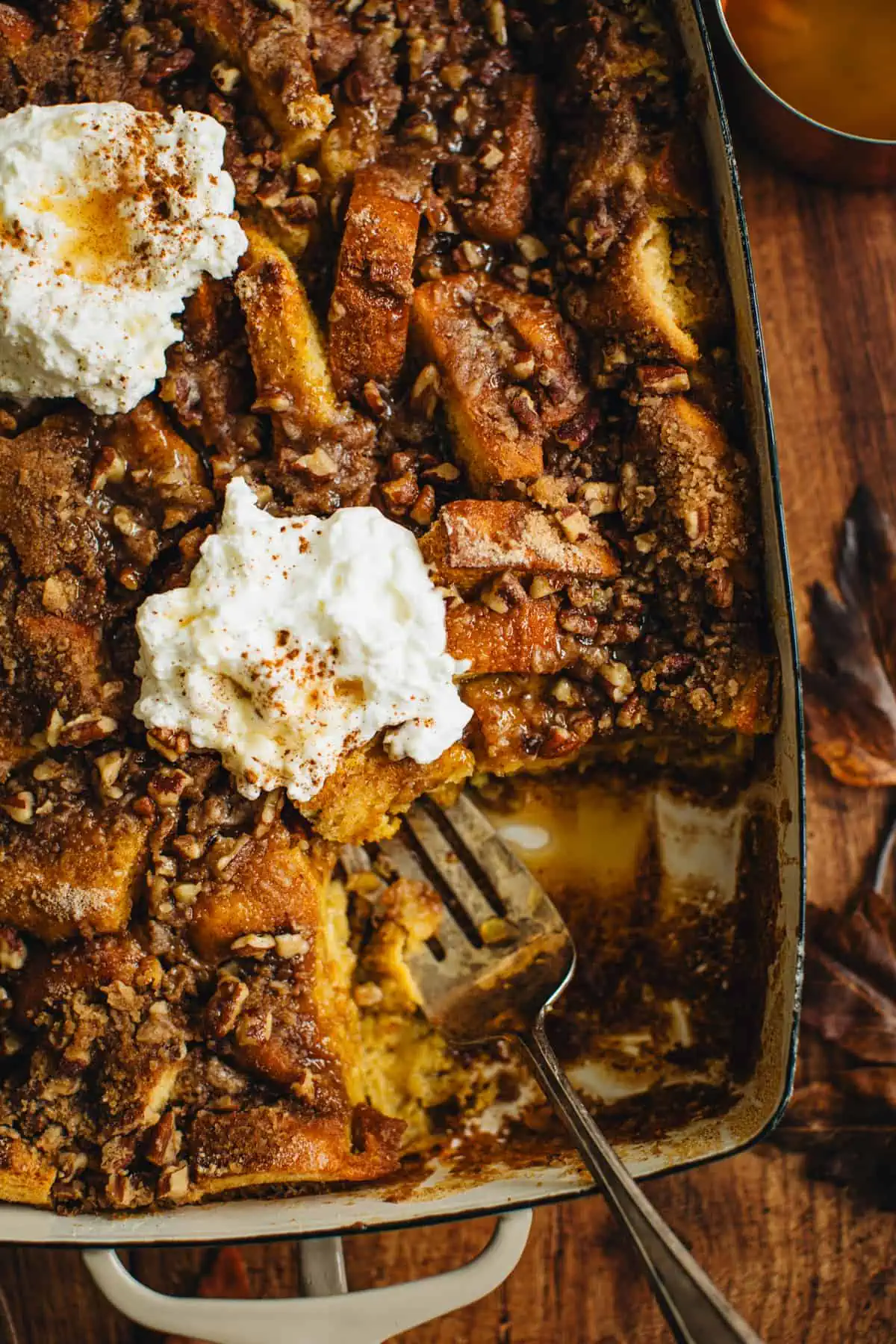 Pumpkin French Toast casserole in a casserole dish topped with whipped cream and a scoop taken out.