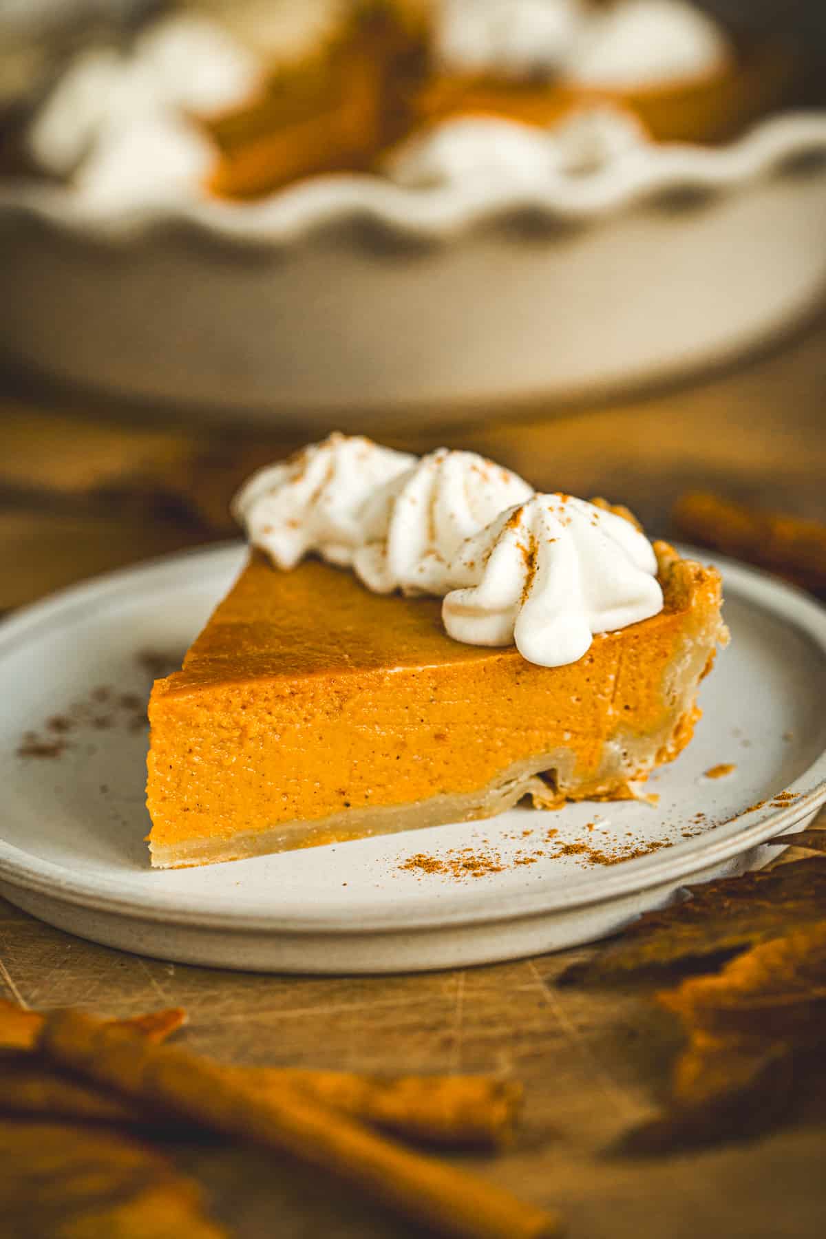 Slice of pumpkin pie topped with whipped cream on a white dessert plate.