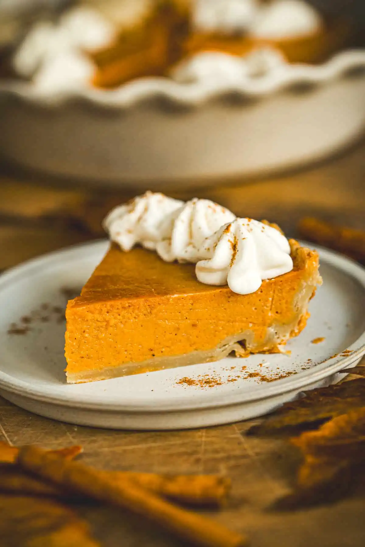 Slice of pumpkin pie topped with whipped cream and cinnamon on a plate.