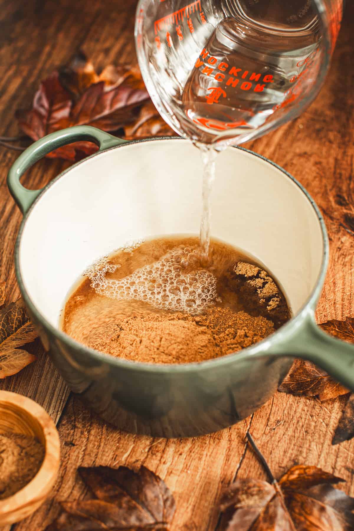 Pouring water into a pot with brown sugar, sugar, and pumpkin pie spice to make Pumpkin Spice Syrup.