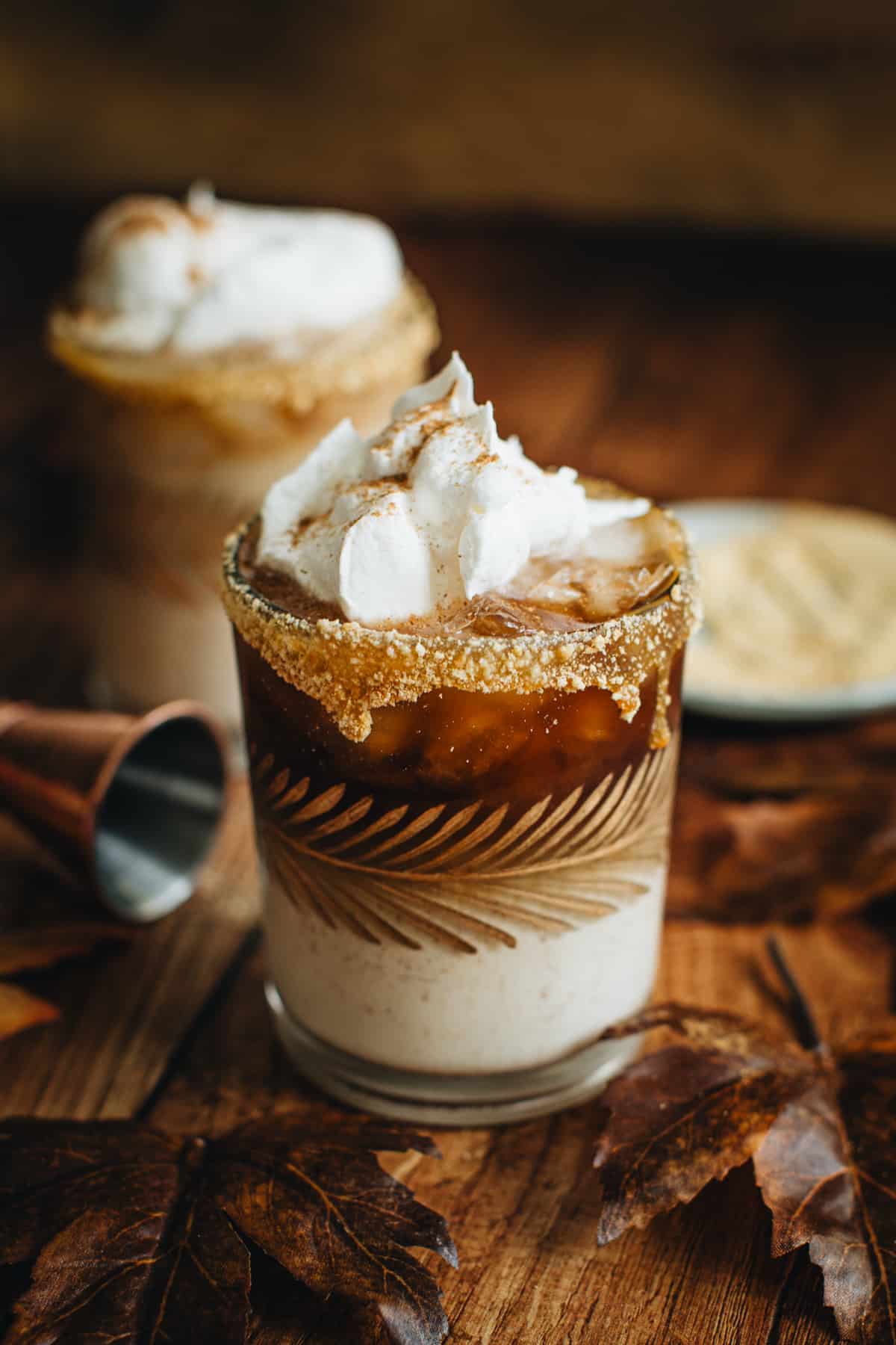 Pumpkin Spice White Russian in a glass topped with whipped cream with a graham cracker coated rim.