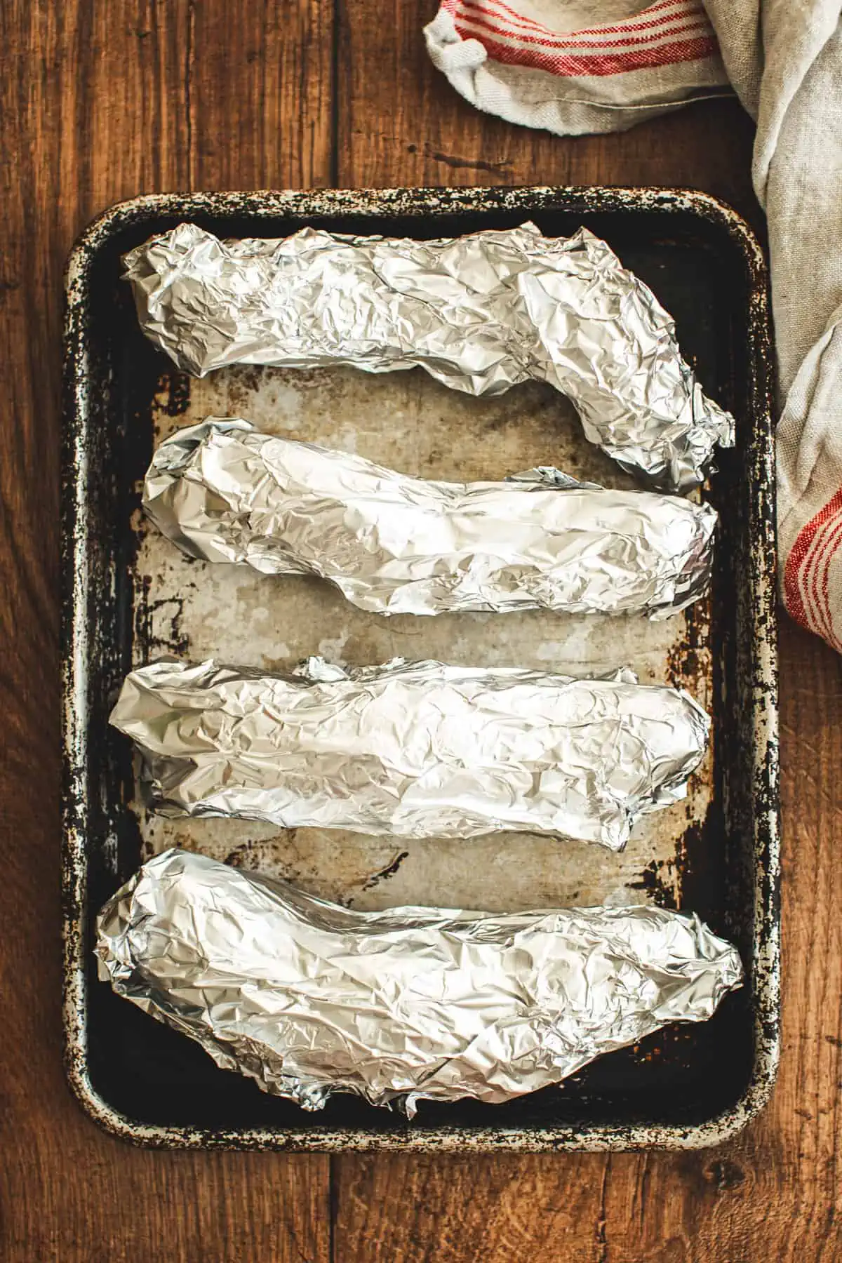 Wrapped potatoes on a rimmed baking sheet for making purple sweet potato pie.