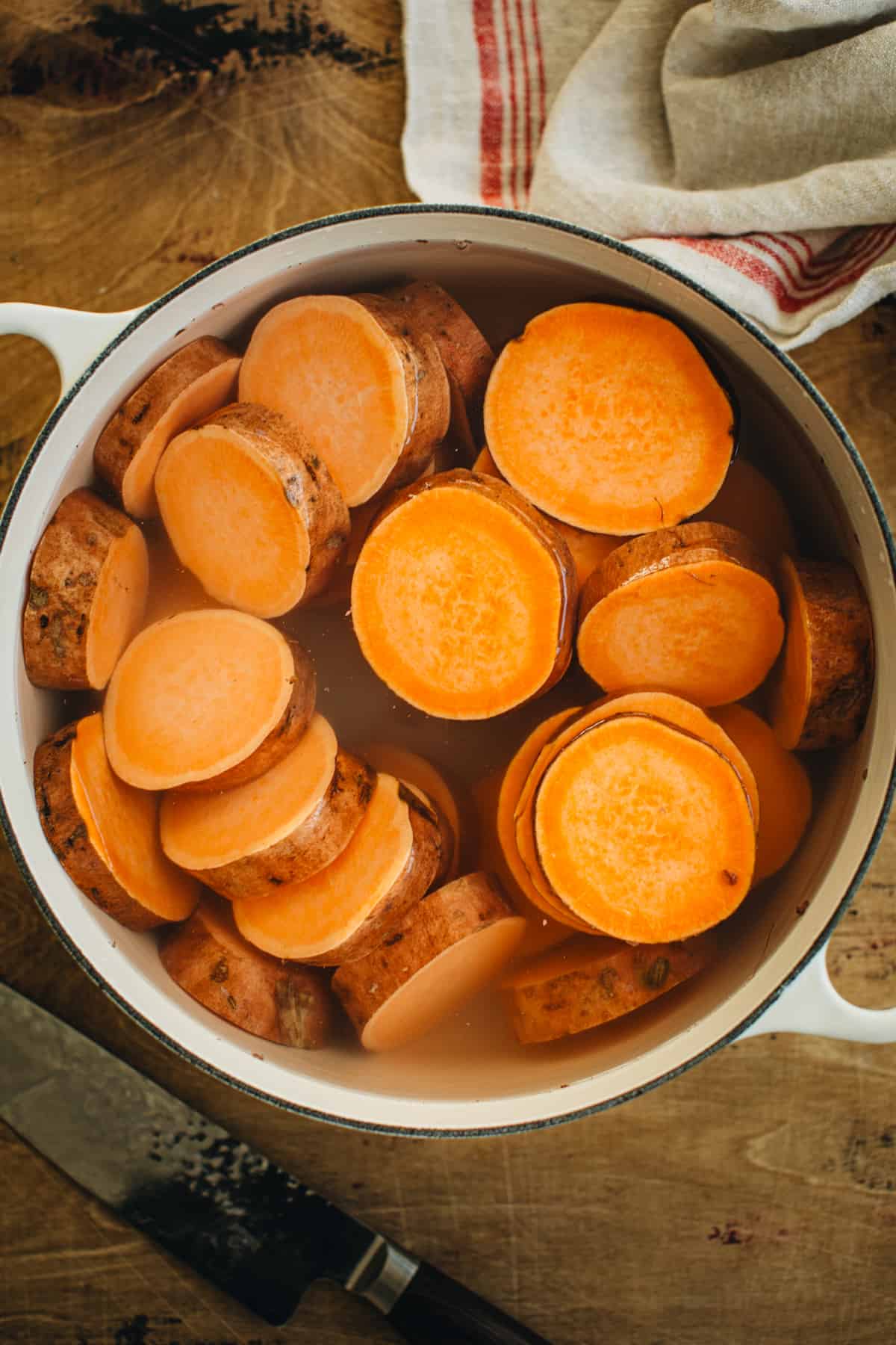 Sliced sweet potatoes in a large pot filled with water ready to boil for making smashed sweet potatoes.