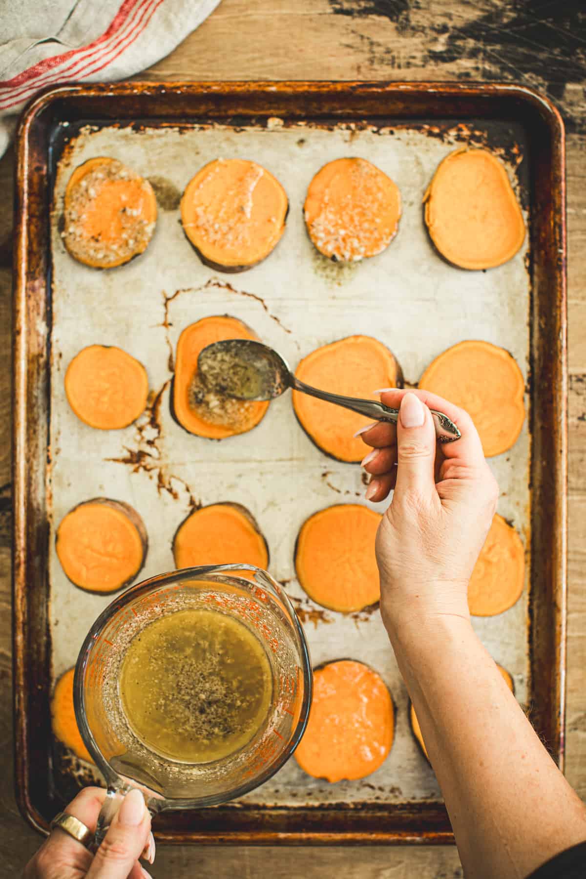 Hand holding a spoon that's drizzling the melted butter over the smashed sweet potatoes.