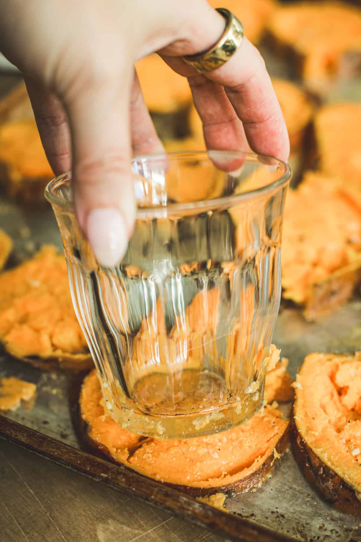 Cup gently smashing sweet potatoes on a rimmed baking sheet for Smashed Sweet Potatoes.