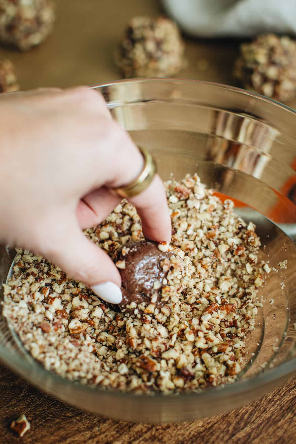 Hand dredging a turtle cooke dough ball into crushed pecans.