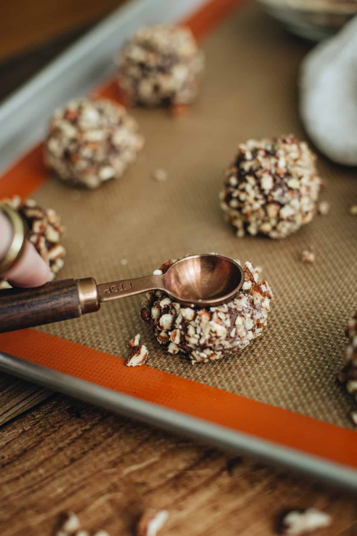 Measuring spoon smashing a turtle cookie dough ball to make the indentation.