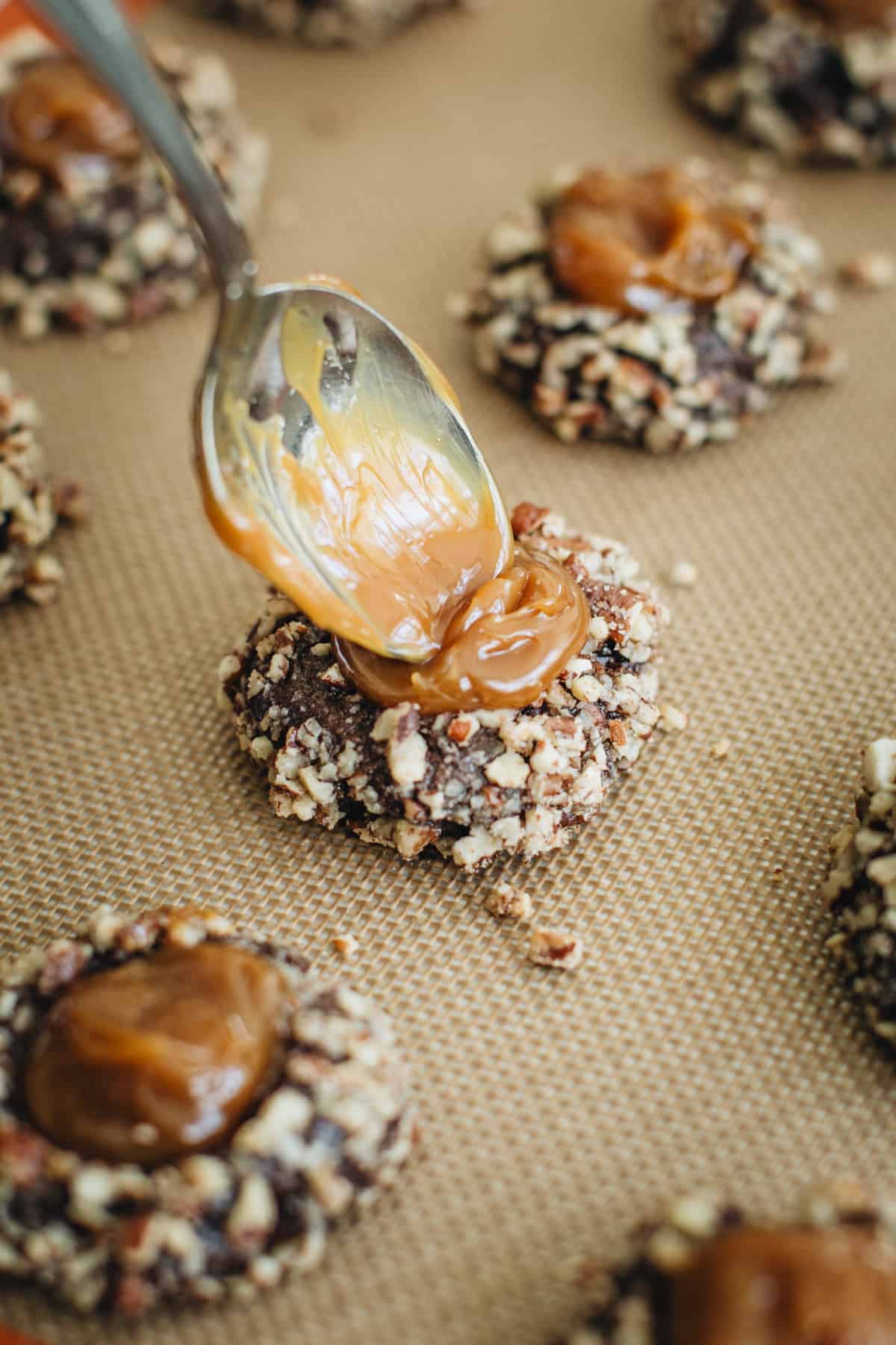 Spoon filling the indentation on a turtle cookie with caramel sauce.