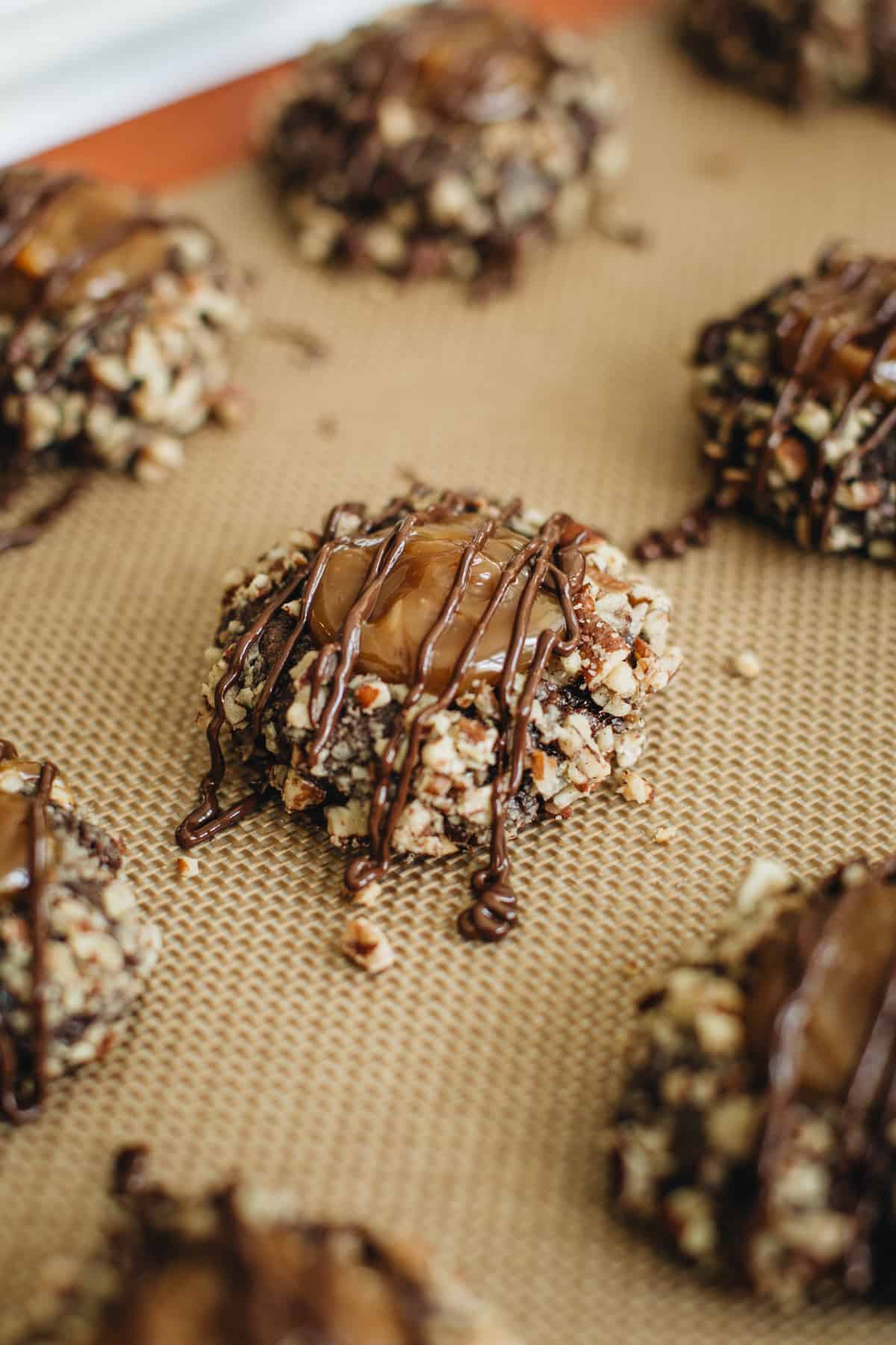 Turtle cookies on a baking sheet drizzled with melted chocolate.