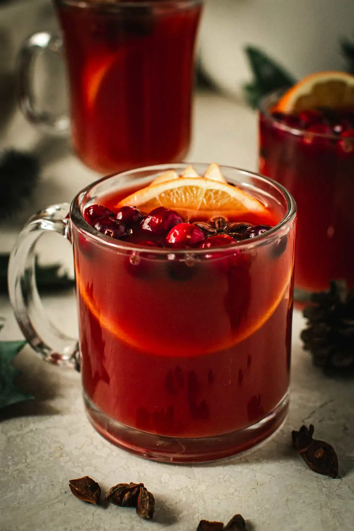 Wassail in a glass mug with fresh cranberries and orange slices for garnish.